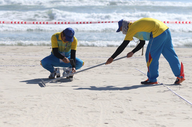 Trọng tài chuẩn bị sân bãi cho buổi thi đấu, trong đó có việc đóng ''khung thành'' xuống cát