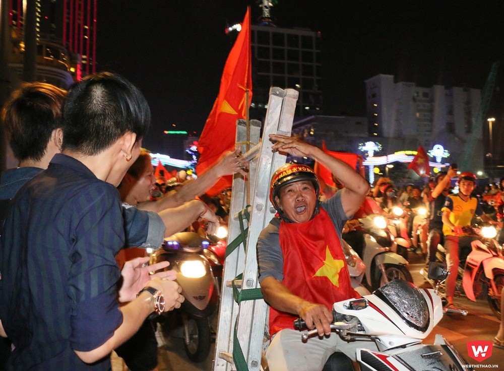 Một người đàn ông đang đi làm về, chở theo chiếc thang cũng hòa cùng dòng người ăn mừng. Ảnh: Quang Thịnh.