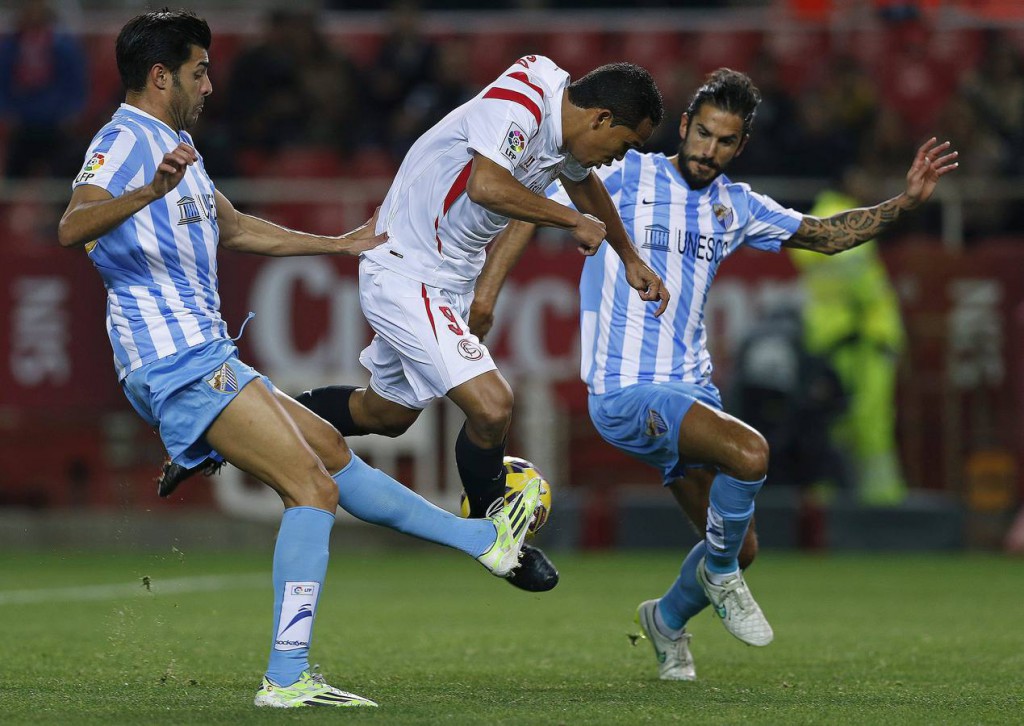 GRA303. SEVILLA, 18/01/2015.- El delantero colombiano del Sevilla, Carlos Arturo Bacca (c), cae ante la entrada de los defensores del Málaga, Miguel Torres (i) y el argentino Marcos Alberto Angeleri, durante el encuentro correspondiente a la jornada diecinueve de primera división, que disputan esta noche en el estadio Sánchez Pizjuán de Sevilla. EFE/Julio Muñoz.